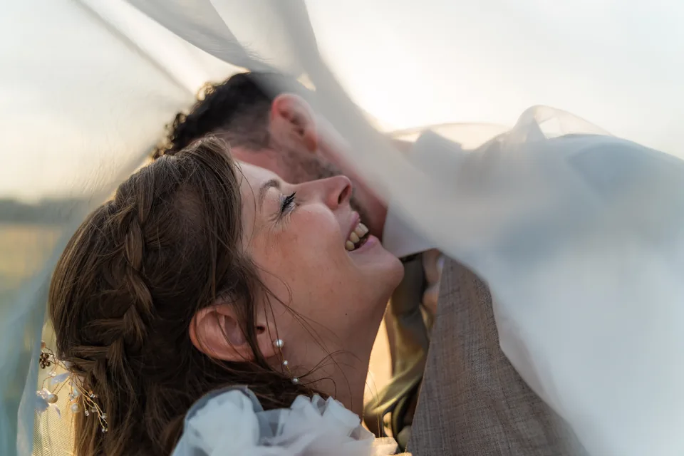 Dinah lacht met haar hoofd tegen Gerard, samen onder haar sluier in het laatste zonlicht