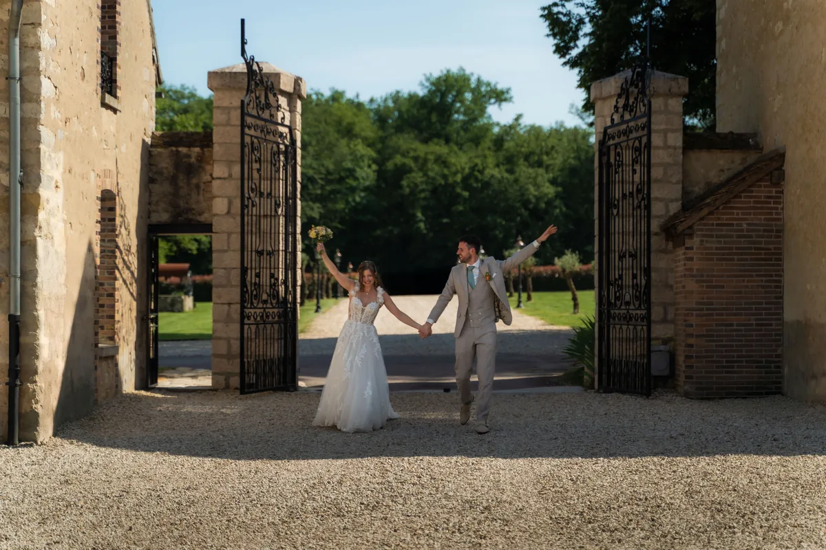 Gerard en Dinah lopen hand in hand en met de armen omhoog door de open smeedijzeren poort tussen de stenen gebouwen