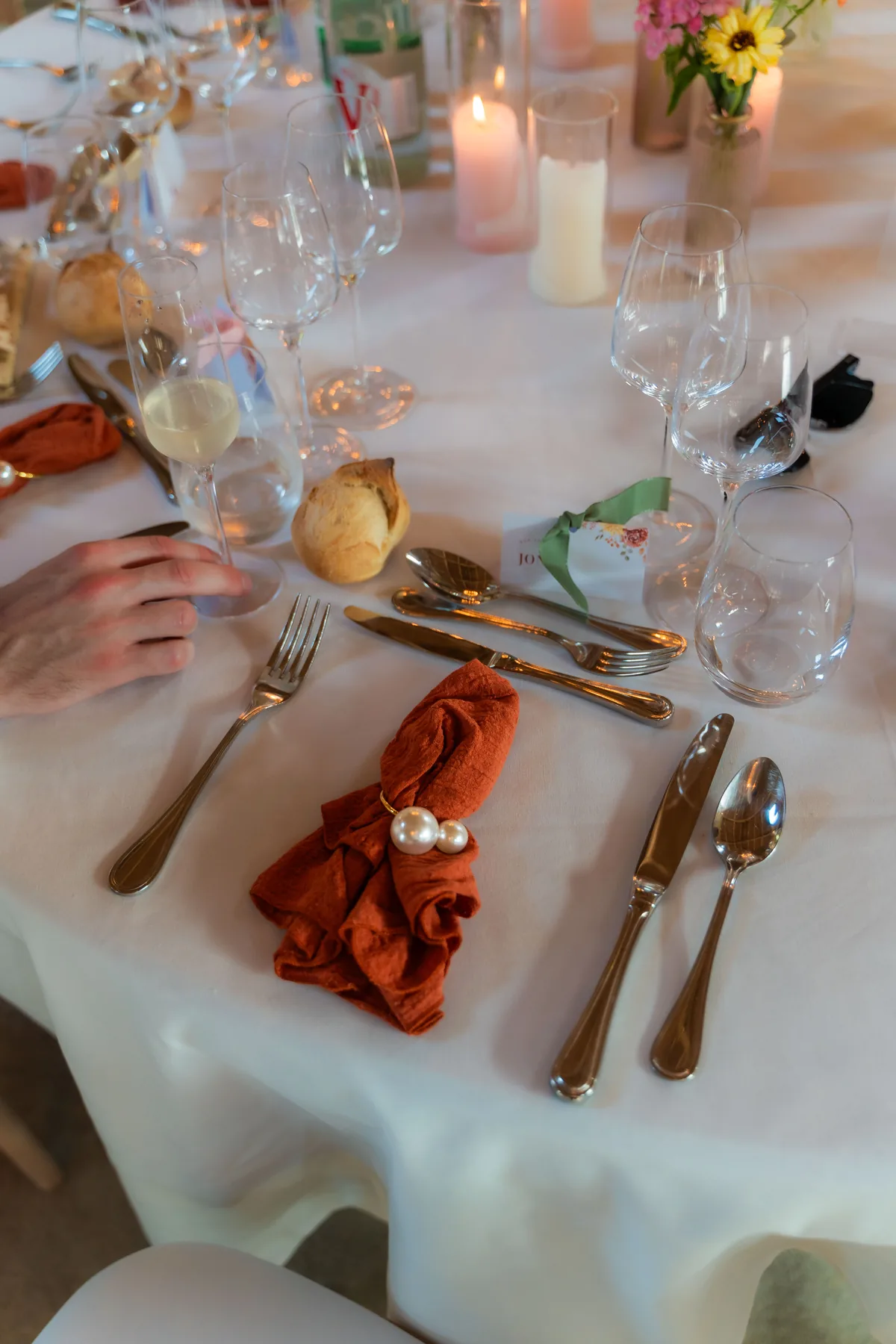 Gedekte ronde tafel met wit tafellaken, glazen, kaarsen en een oranje servet