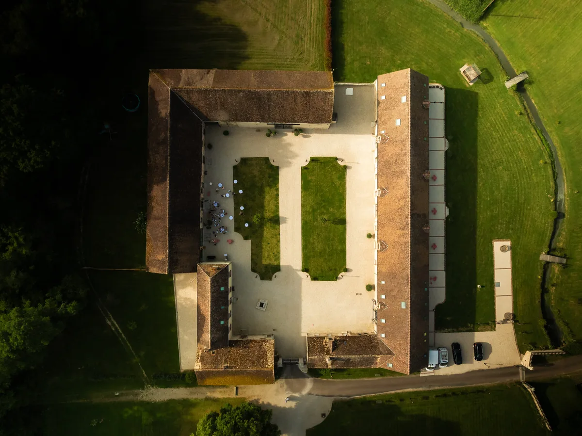 Luchtfoto recht van boven van Domaine de Chenevière: boerderijgebouwen met pannendaken rondom een binnenplaats met twee grasvelden
