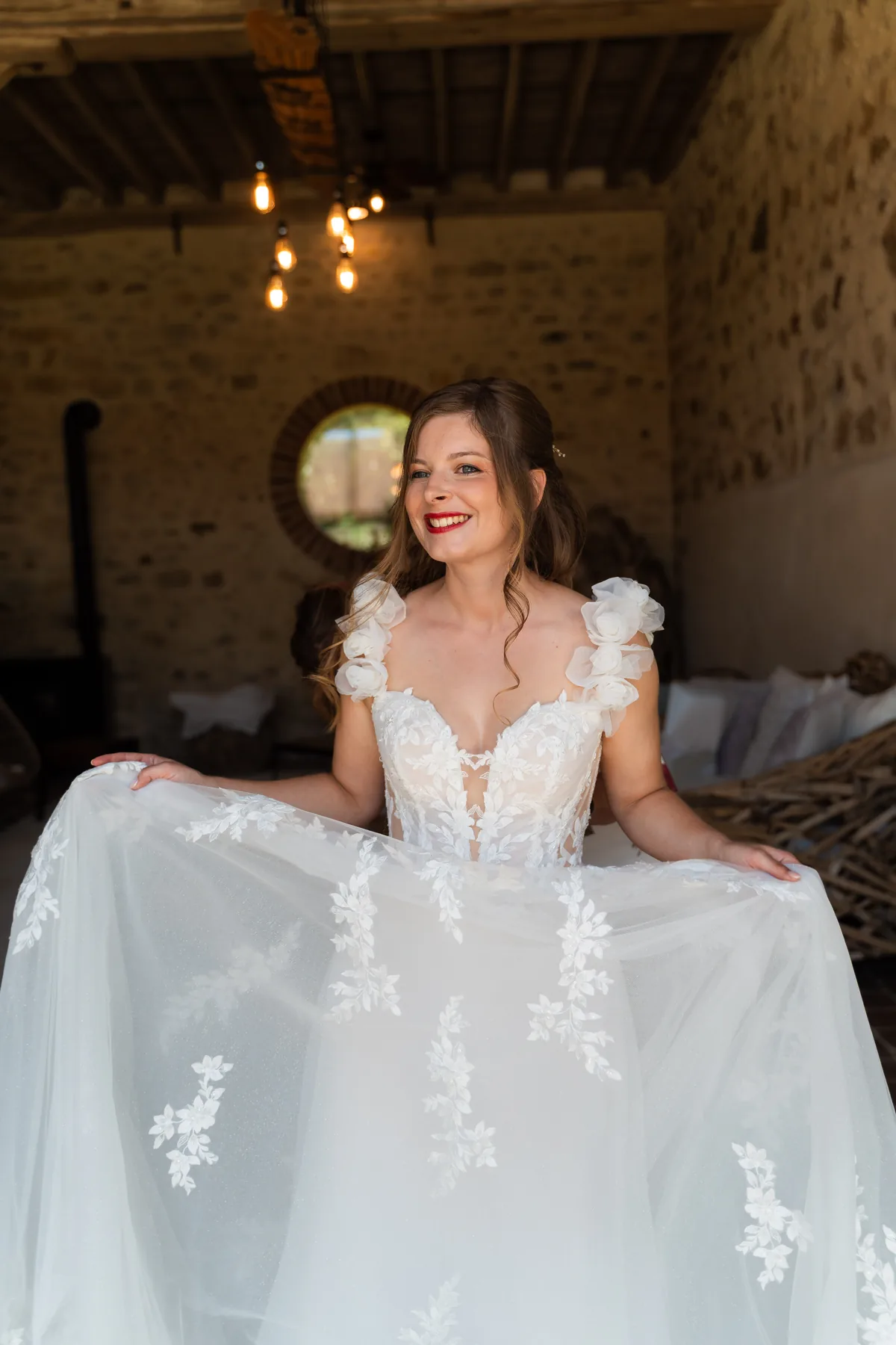 Dinah in haar trouwjurk, lachend met de rok in haar handen, in een ruimte met natuurstenen muren en een rond raam