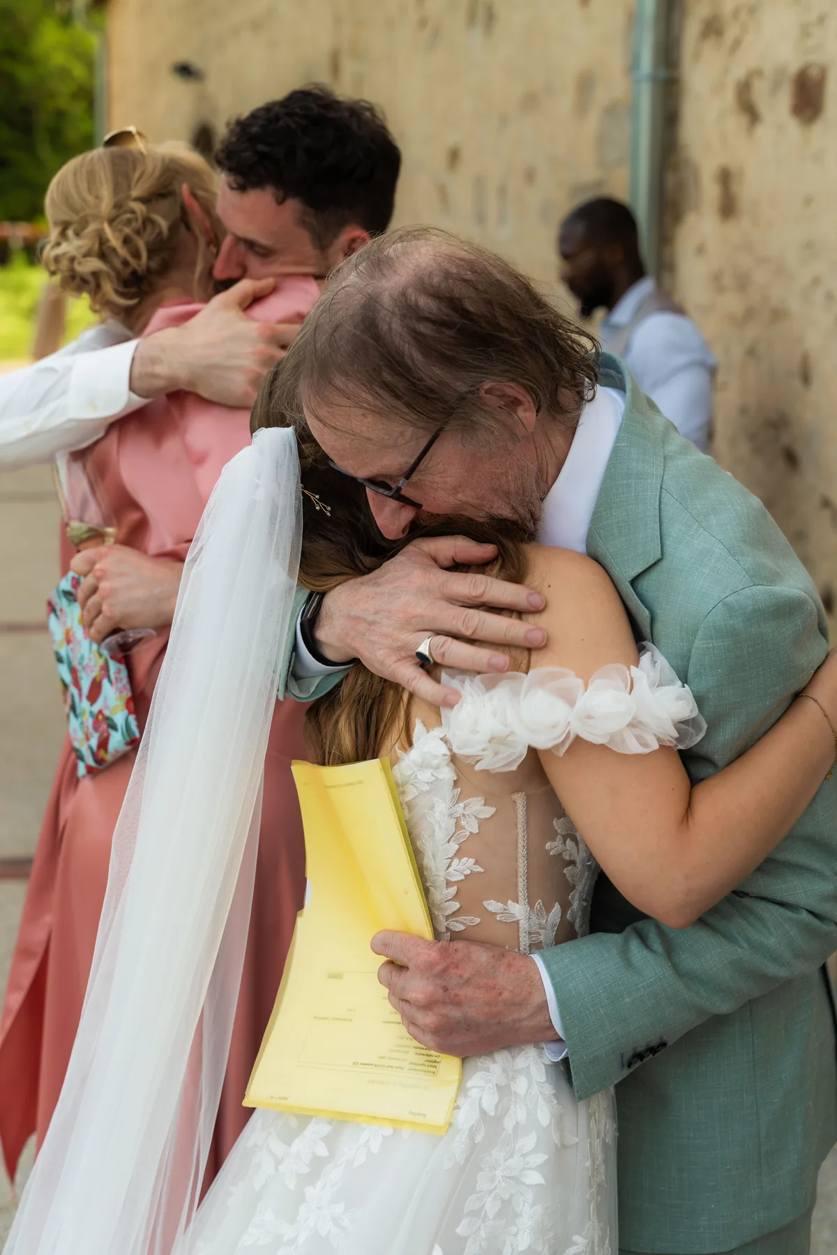 Dinah wordt stevig omhelsd door een oudere man met een geel papier in zijn hand
