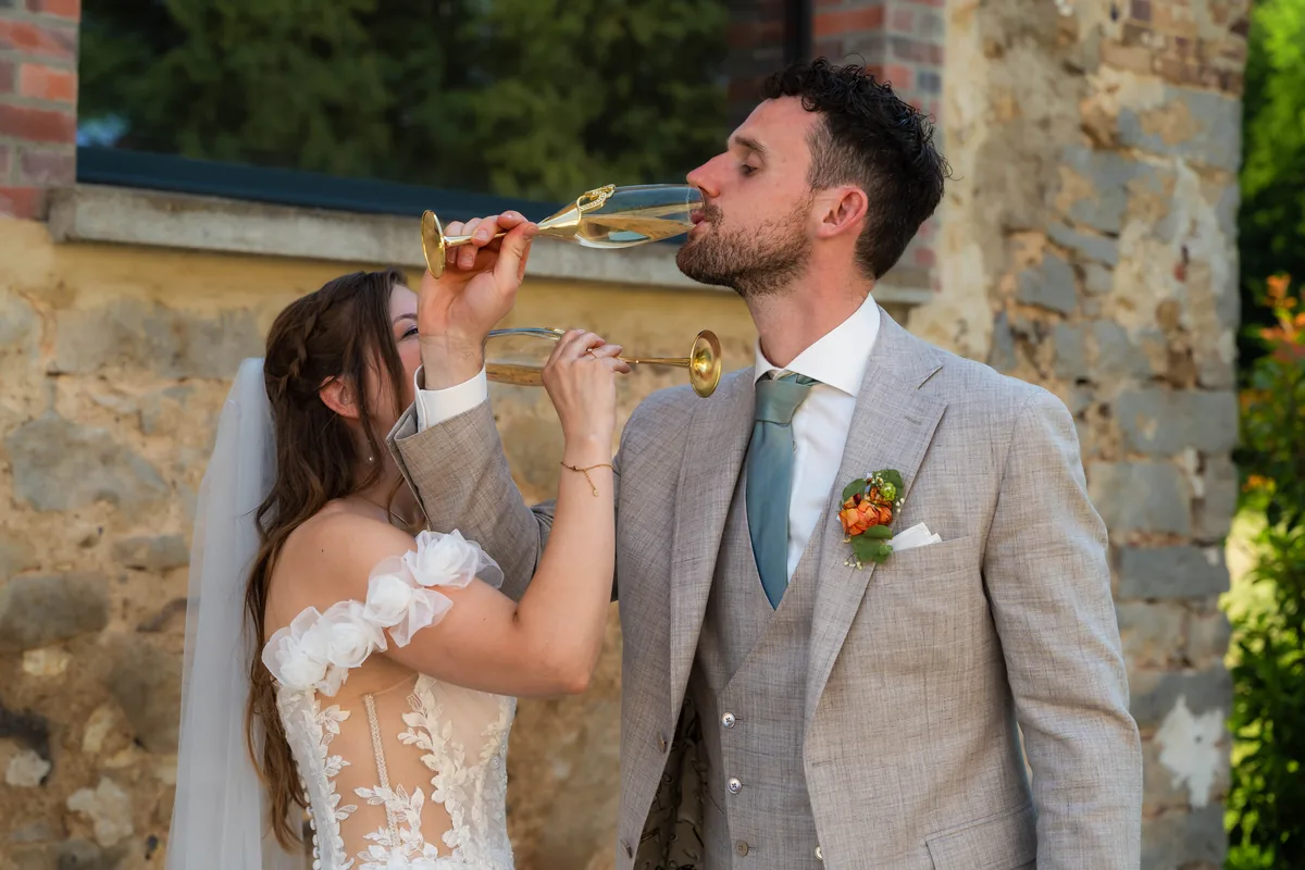 Gerard en Dinah drinken met gekruiste armen champagne voor een stenen muur