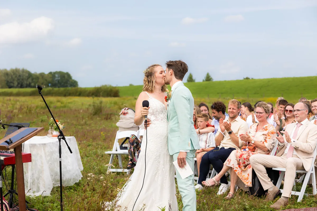 Jelle en Deborah kussen tijdens de ceremonie, met de gasten op de achtergrond