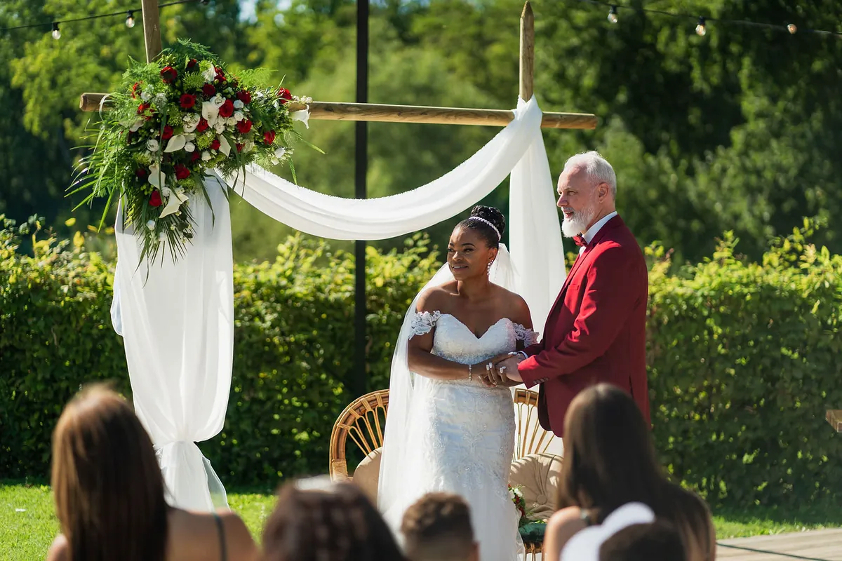 Lizita en Martino tijdens de ceremonie onder een boog met bloemen