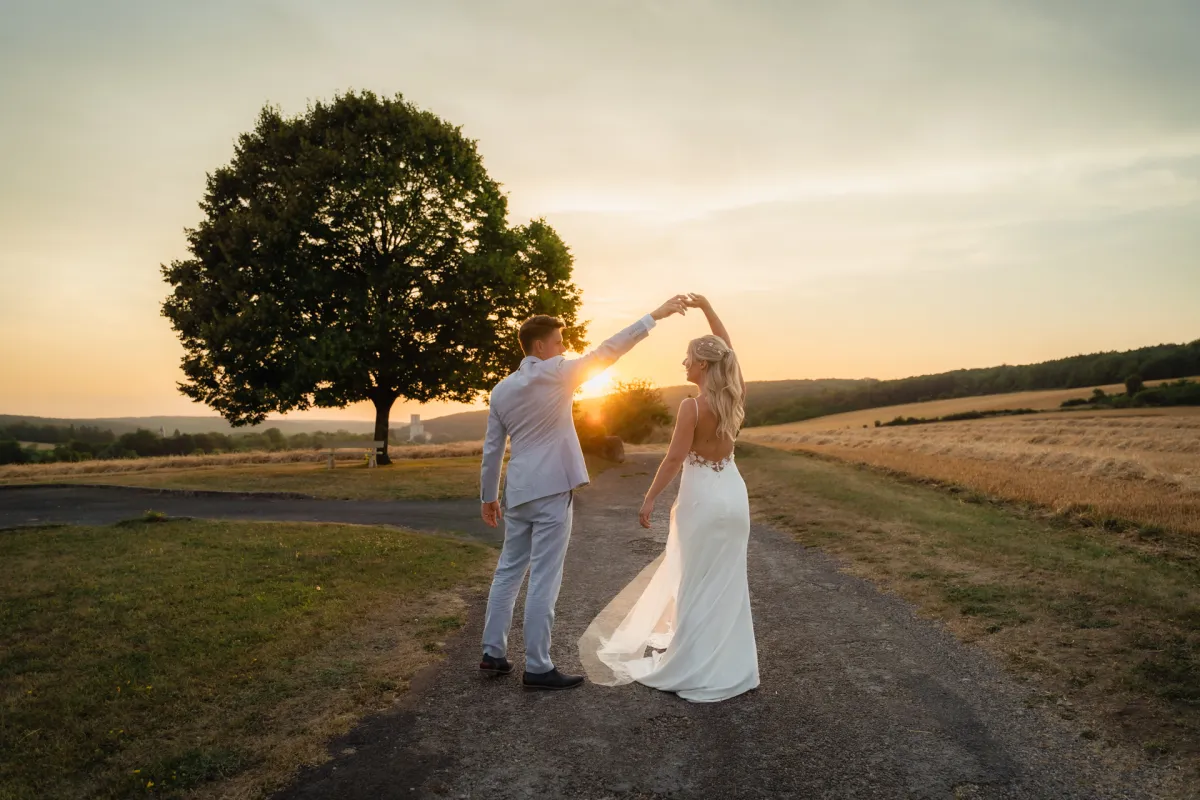 Bruidspaar danst hand in hand op een landelijk pad bij zonsondergang