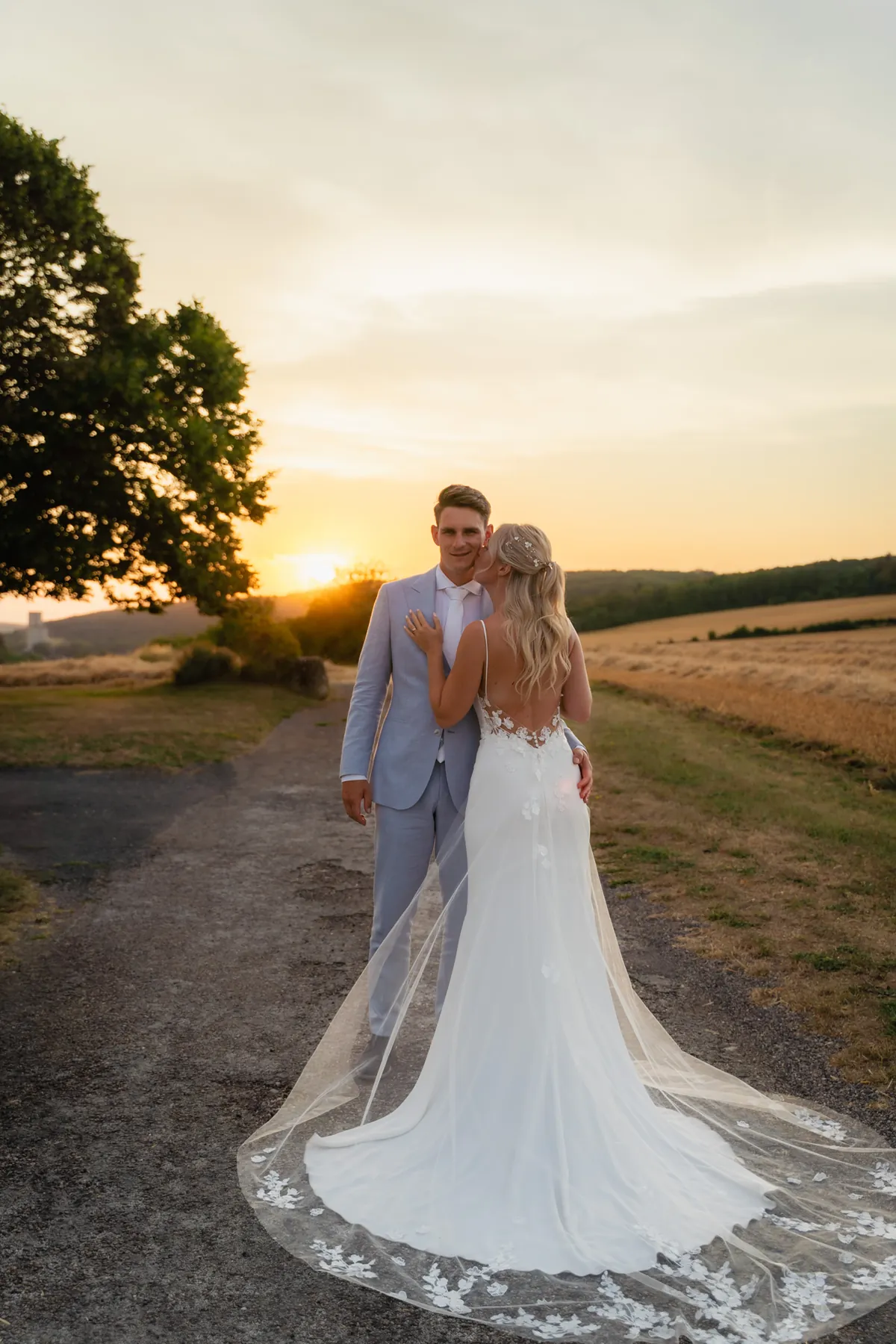 Bruidspaar hand in hand op een landelijk pad bij zonsondergang, met een warme en sfeervolle achtergrond