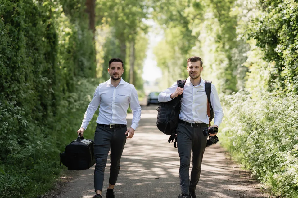 Een fotograaf en videograaf Marco van WeddingGuys lopen over een pad tussen groene heggen