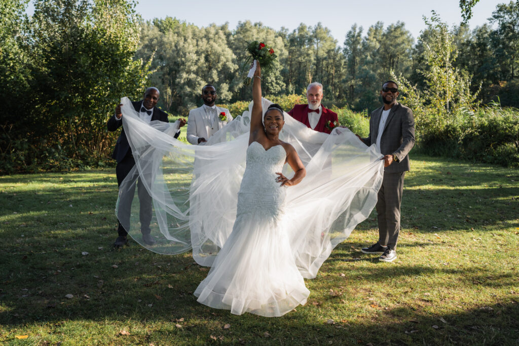 Bruid poseert in haar trouwjurk met sluier omhoog, omringd door bruidegom en groomsmen bij Lake House Rotterdam