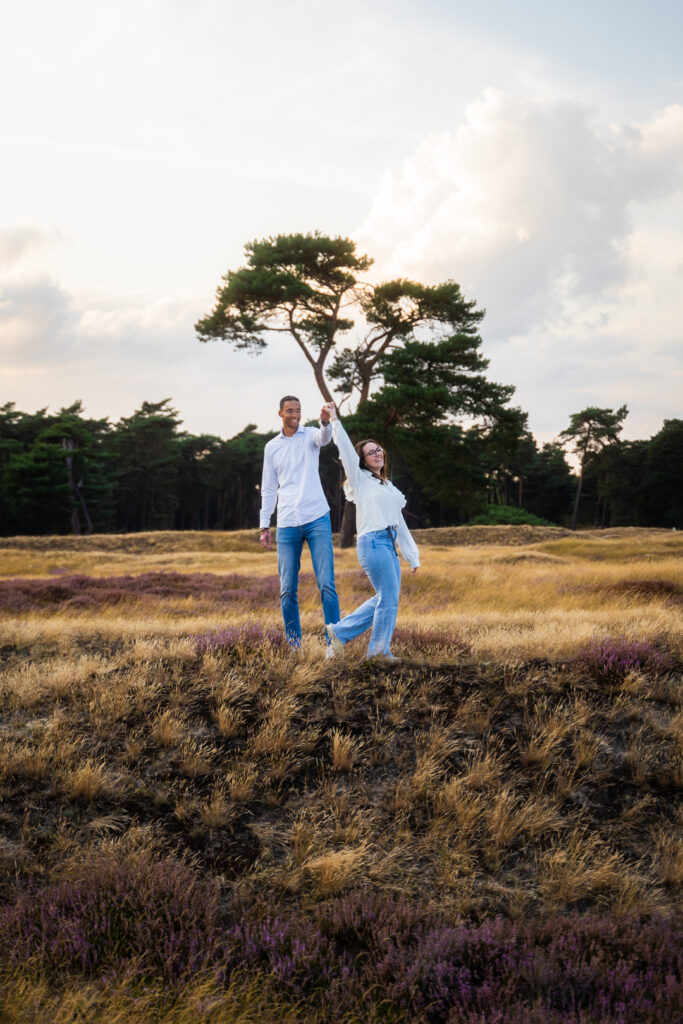 Romantische pre-wedding fotoshoot van een aanstaand bruidspaar waarbij de man de vrouw ronddraait in een open landschap.